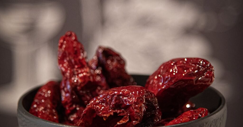 A rustic black bowl filled with vibrant red dried jujubes on a marble surface.
