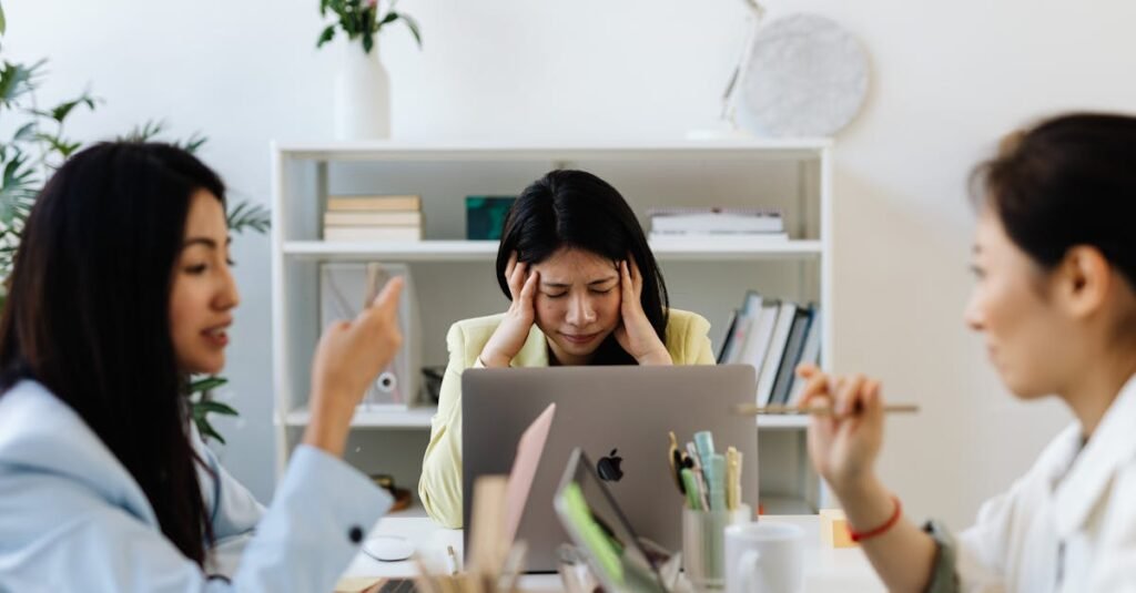 Asian businesswoman dealing with job stress in a modern office environment, surrounded by colleagues.